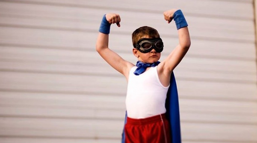 Small boy in homemade super hero costume. Costume includes cape, swimming googles, white tank top and red shorts.